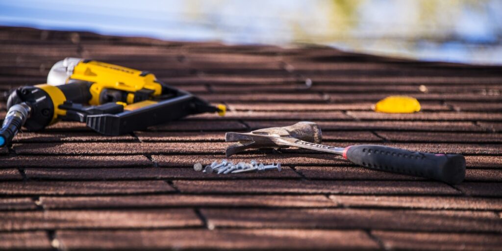 An image of a nail gun, hammer, and nails resting on a roof.