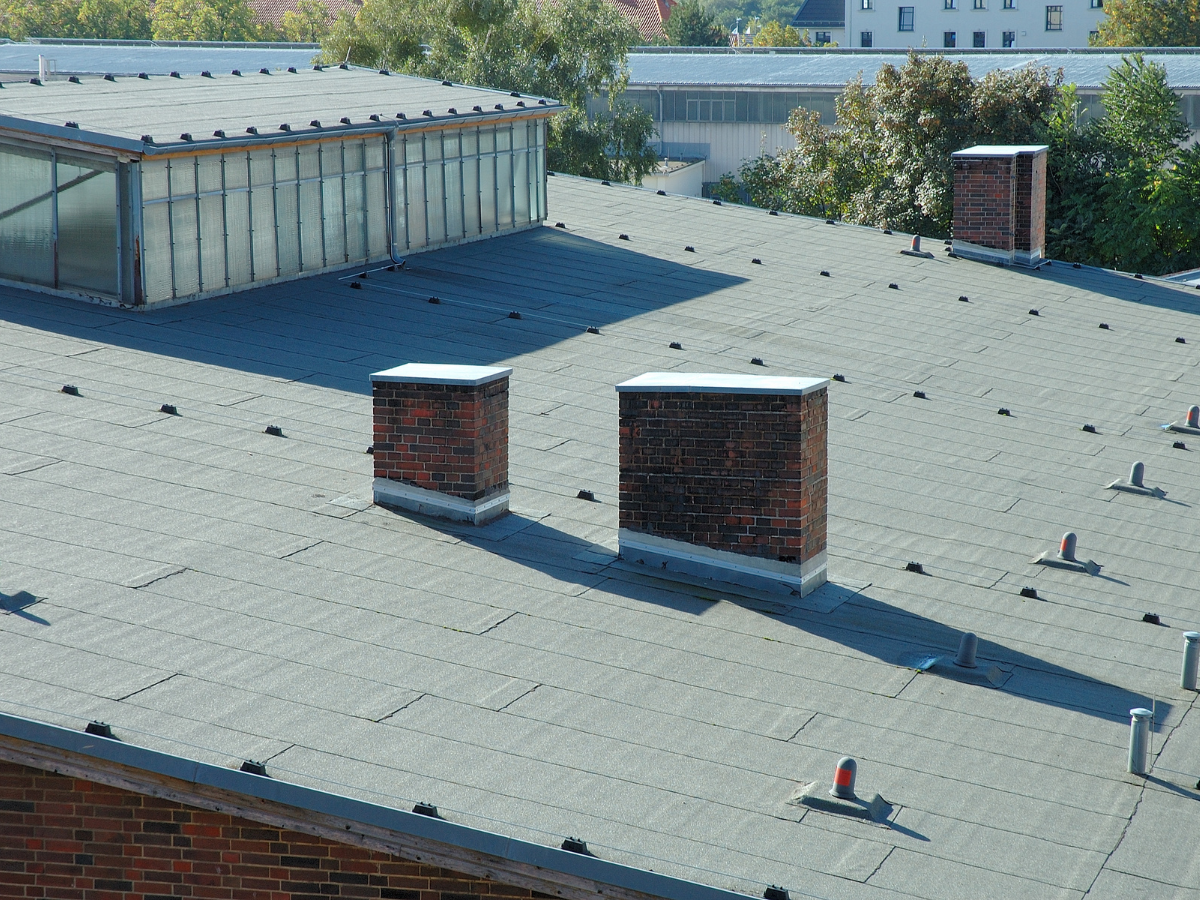 Flat commercial roof with a clean, smooth surface, featuring two brick chimneys and various ventilation units.