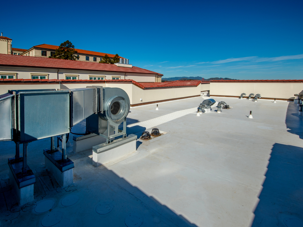 Commercial rooftop with HVAC units and vents, featuring a clean, flat roof surface, with a building and clear sky in the background.