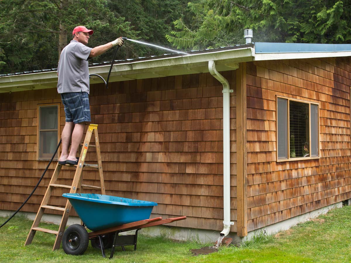 Man on ladder spraying gutters with a hose