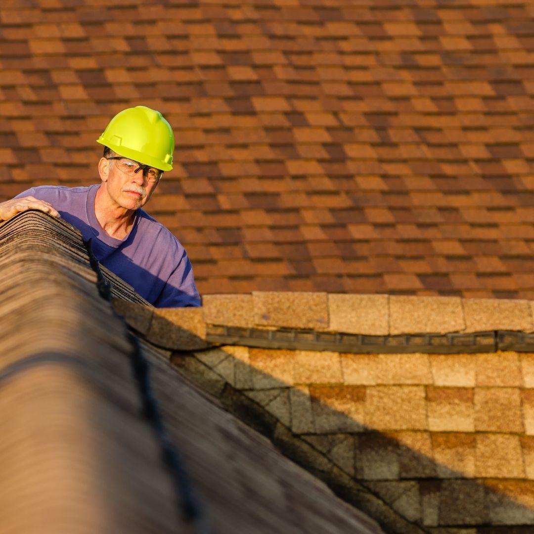 A roofer in a hard hat peers over a roof and inspects it