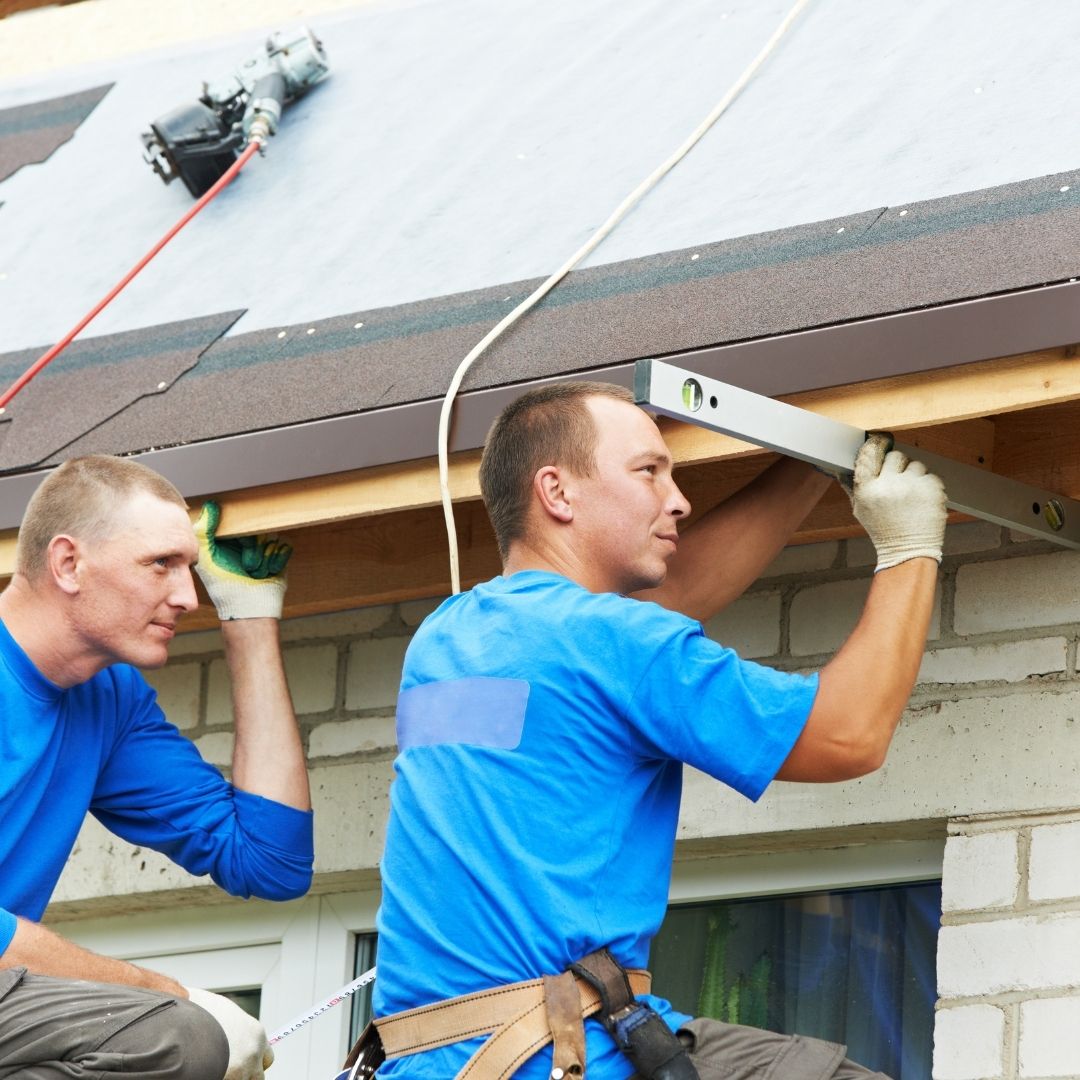 Two roofing contractors working on installing soffit on a building