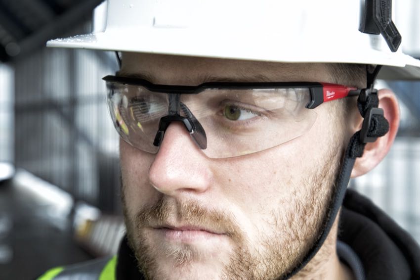 man wearing safety glasses and hard hat. He has a red mustache and beard and fair skin.